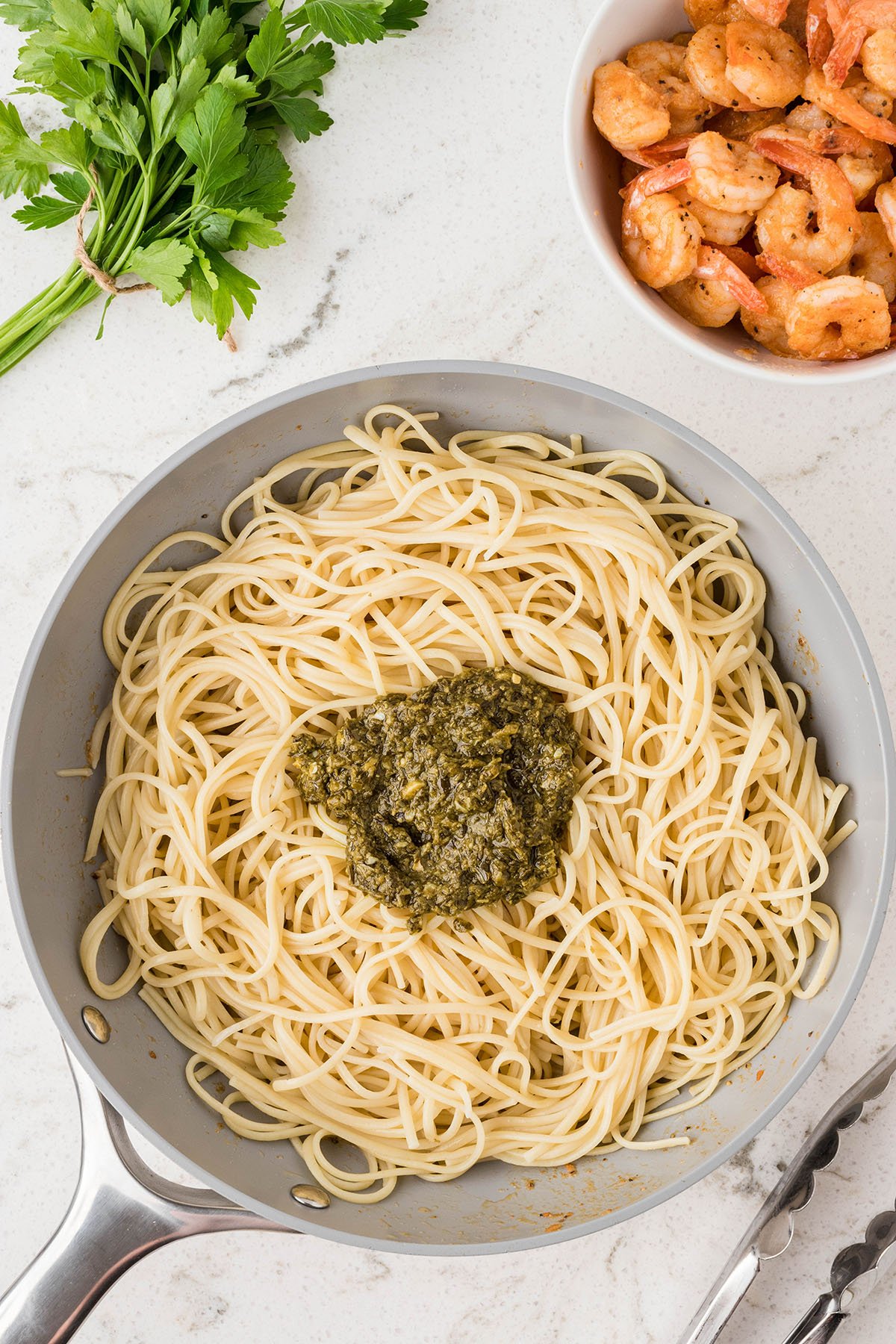 Pesto is added to the linguine in the skillet.