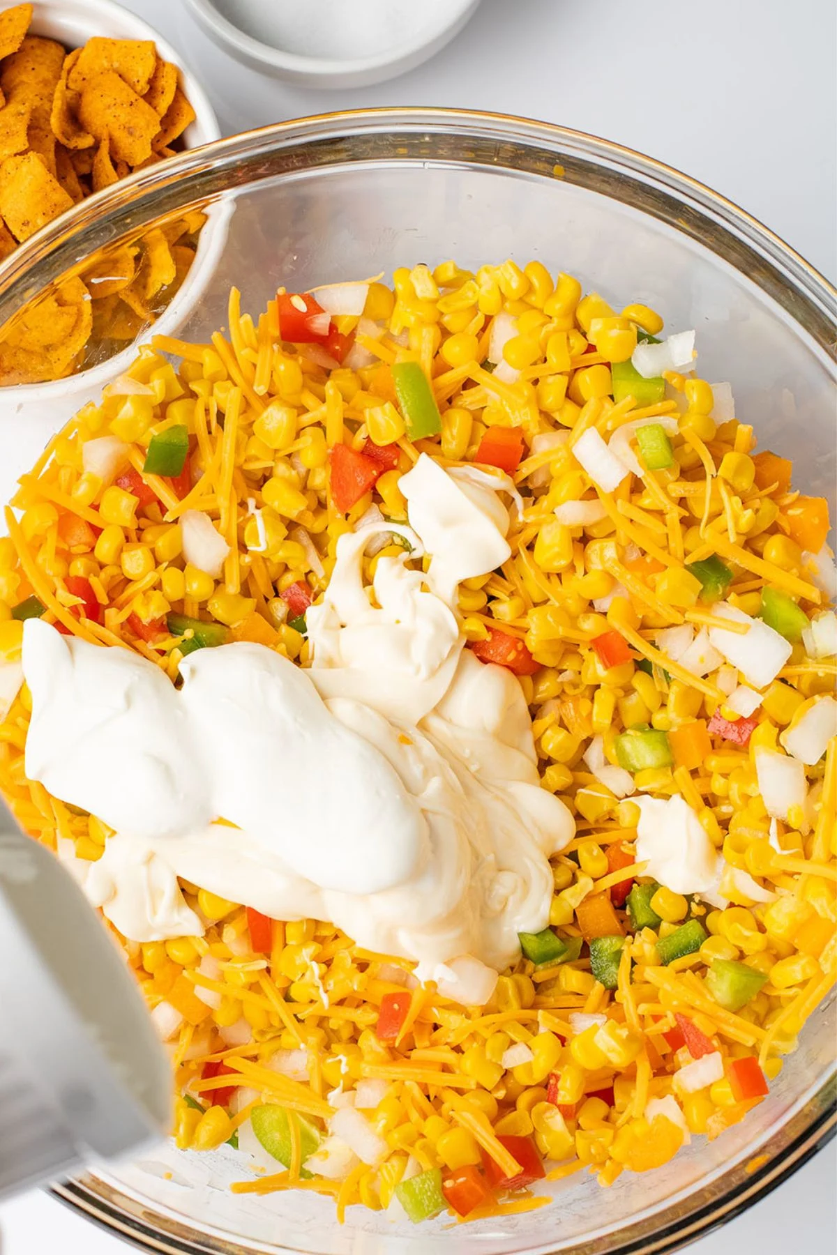 Sour cream and mayonnaise are added to the vegetables in the glass mixing bowl.