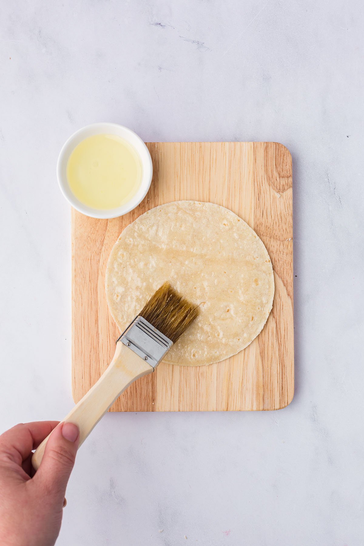 Tortillas are brushed with oil on a wooden cutting board.