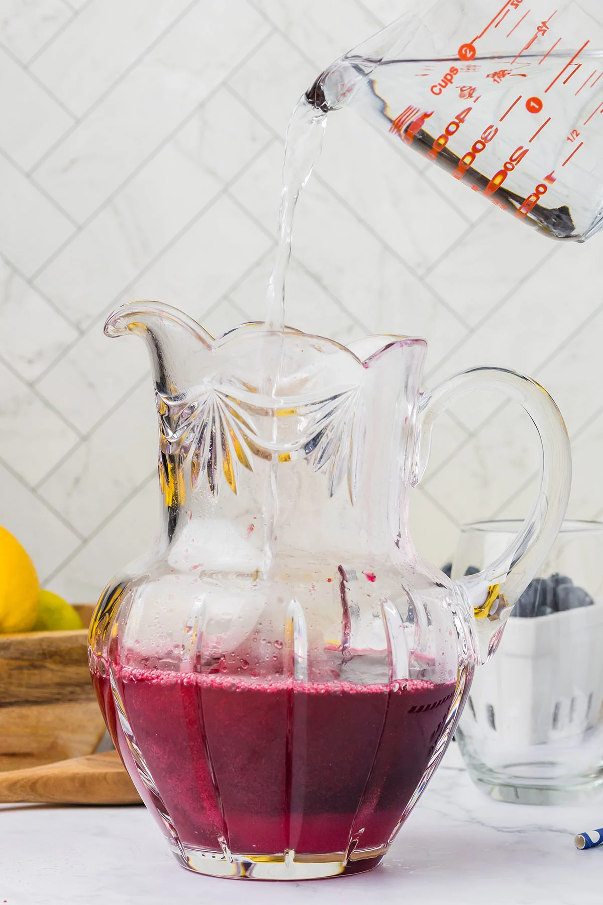 Water is poured into the blueberry lemonade in the glass pitcher.