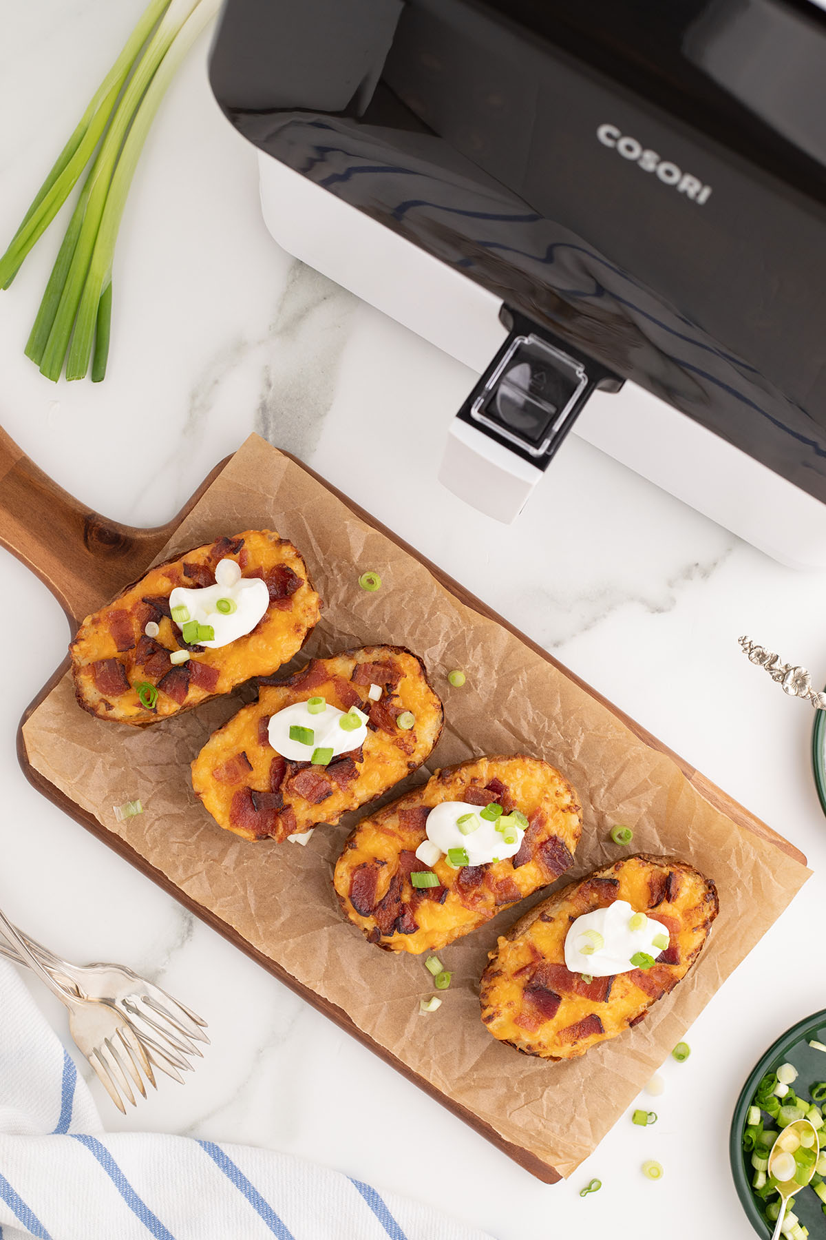 Twice Baked Potatoes topped with sour cream on a parchment paper lined wooden board.
