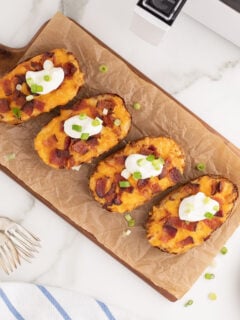 Air Fryer Twice Baked Potatoes on a parchment paper lined wooden serving board.
