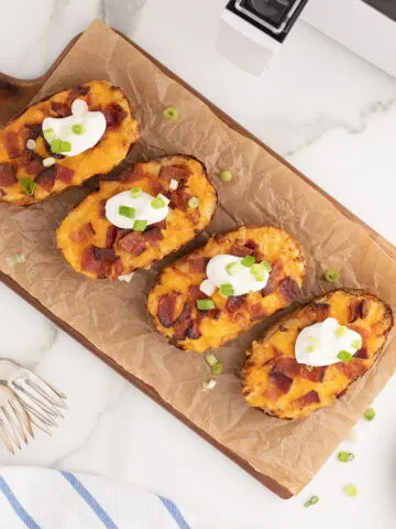 Air Fryer Twice Baked Potatoes on a parchment paper lined wooden serving board.