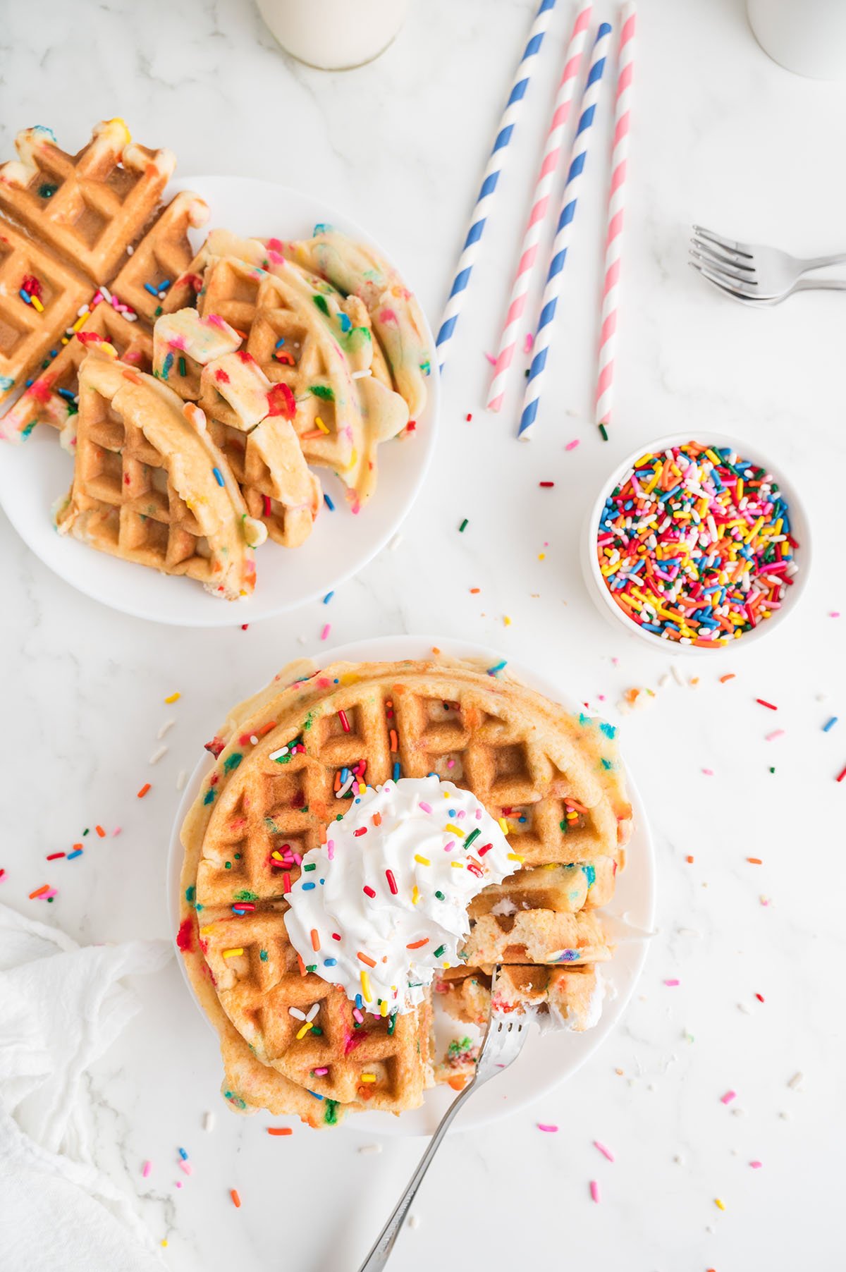 Birthday Cake Waffle topped with whipped cream and sprinkles on a plate with a bite on a fork.