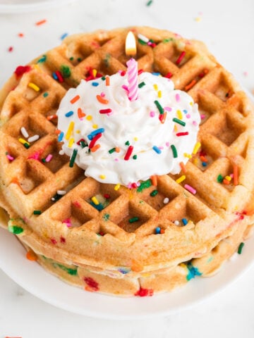 Birthday Cake Waffles on a plate topped with whipped cream, sprinkles, and a candle.