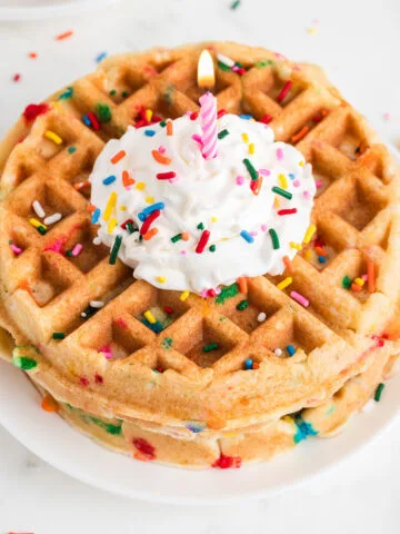 Birthday Cake Waffles on a plate topped with whipped cream, sprinkles, and a candle.