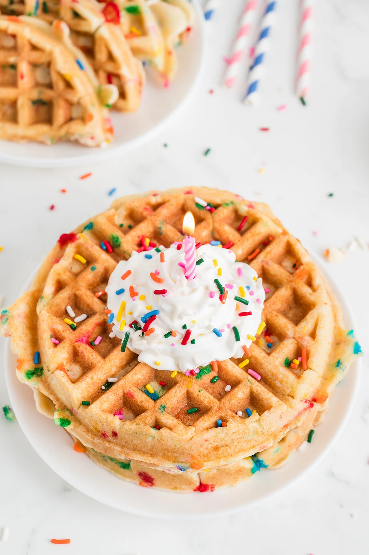 Birthday Cake Waffles topped with whipped cream, sprinkles, and a candle on a plate.
