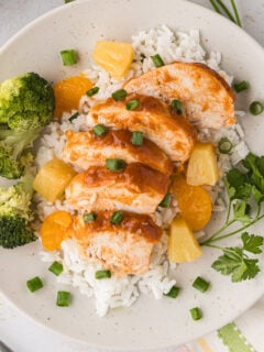 Hawaiian chicken is sliced and served over rice on a plate.