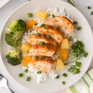 Hawaiian chicken is sliced and served over rice on a plate.