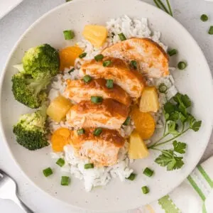 Hawaiian chicken is sliced and served over rice on a plate.