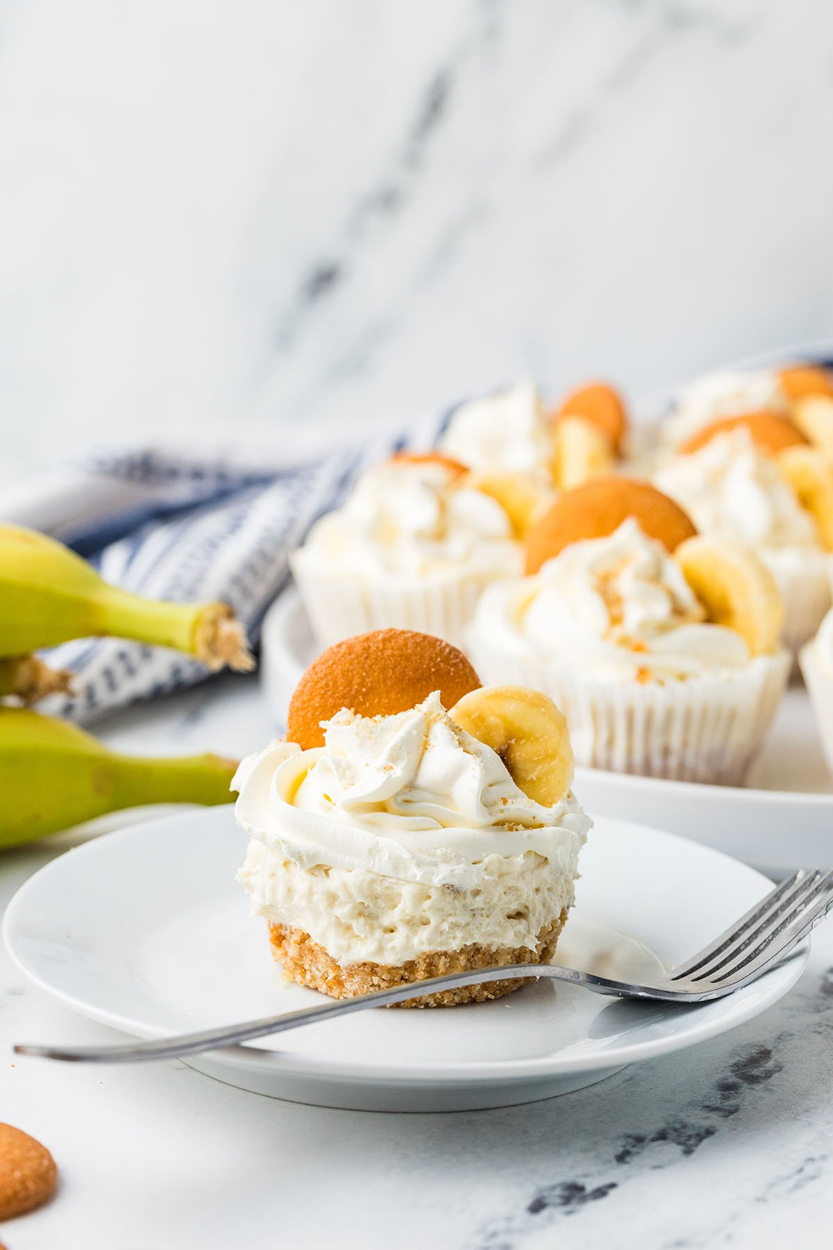 Mini Banana Cheesecakes served on a white plate, topped with a vanilla wafer and a slice of banana.
