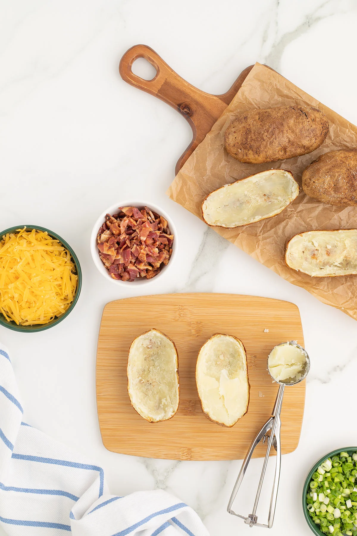 Baked potatoes are cut in half, and the insides of the potatoes are scooped out into a bowl.