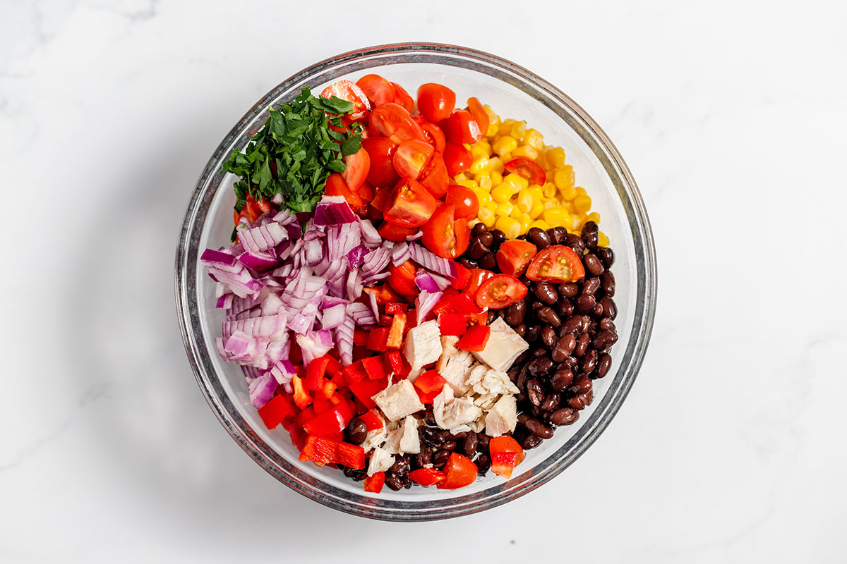 Chicken, black beans, corn, onions, tomatoes, red bell pepper, and cilantro in a glass mixing bowl.