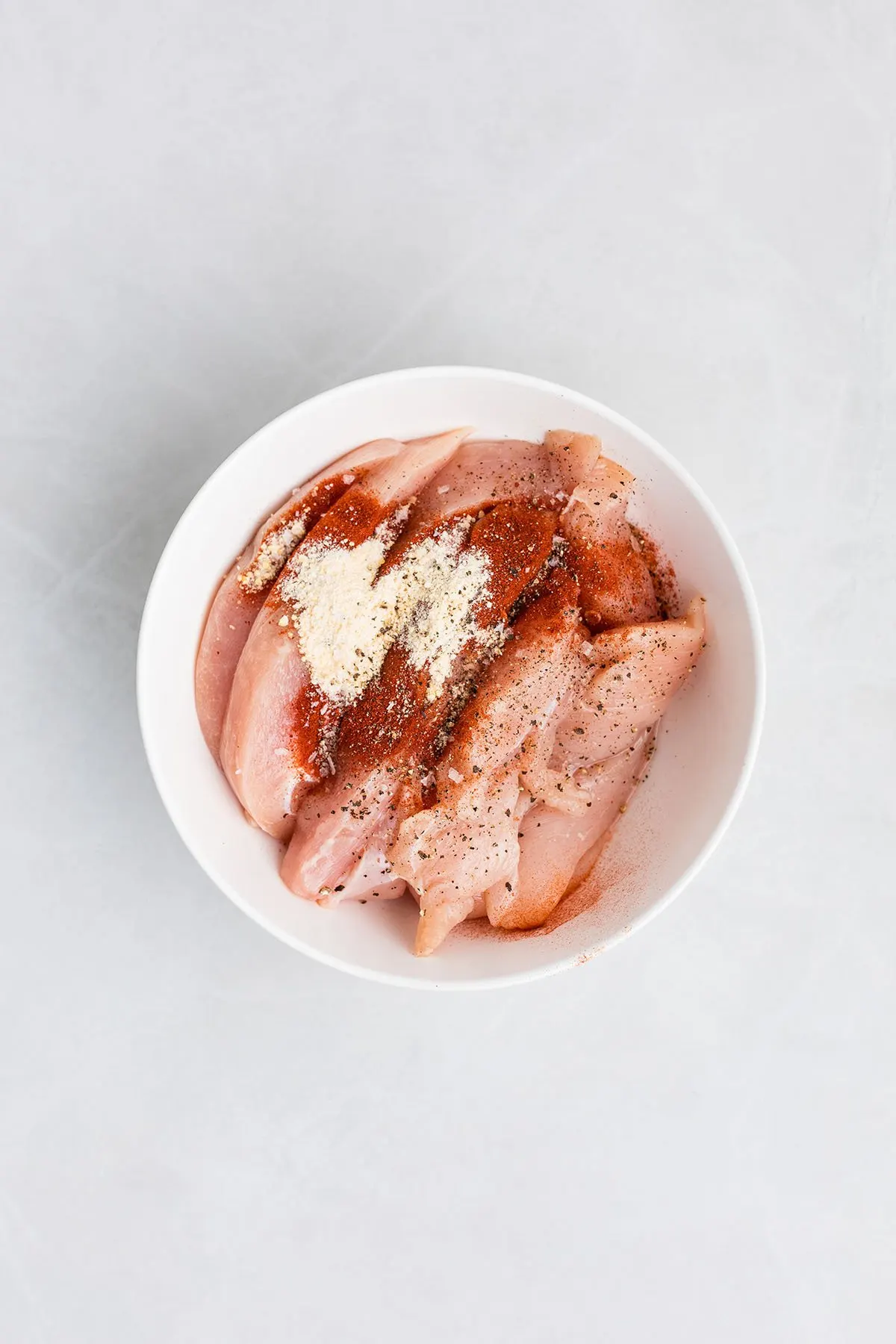 Chicken, garlic powder, smoked paprika, salt, and pepper in a bowl.