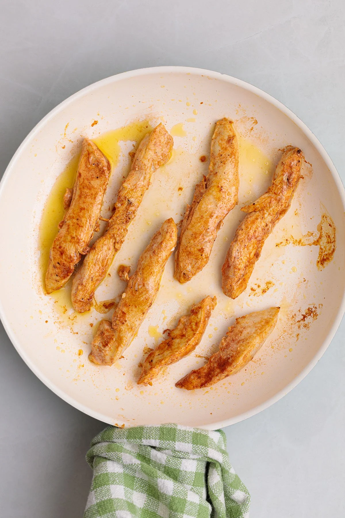 Cooked seasoned chicken strips on a plate.
