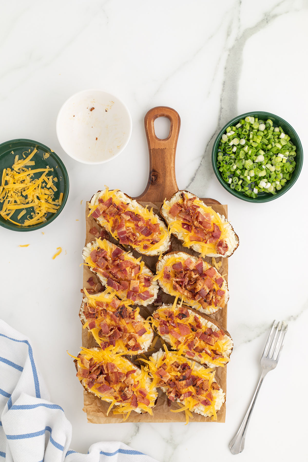Crisp bacon added over the cheese and potato mixture in the potato skins on a wooden board.