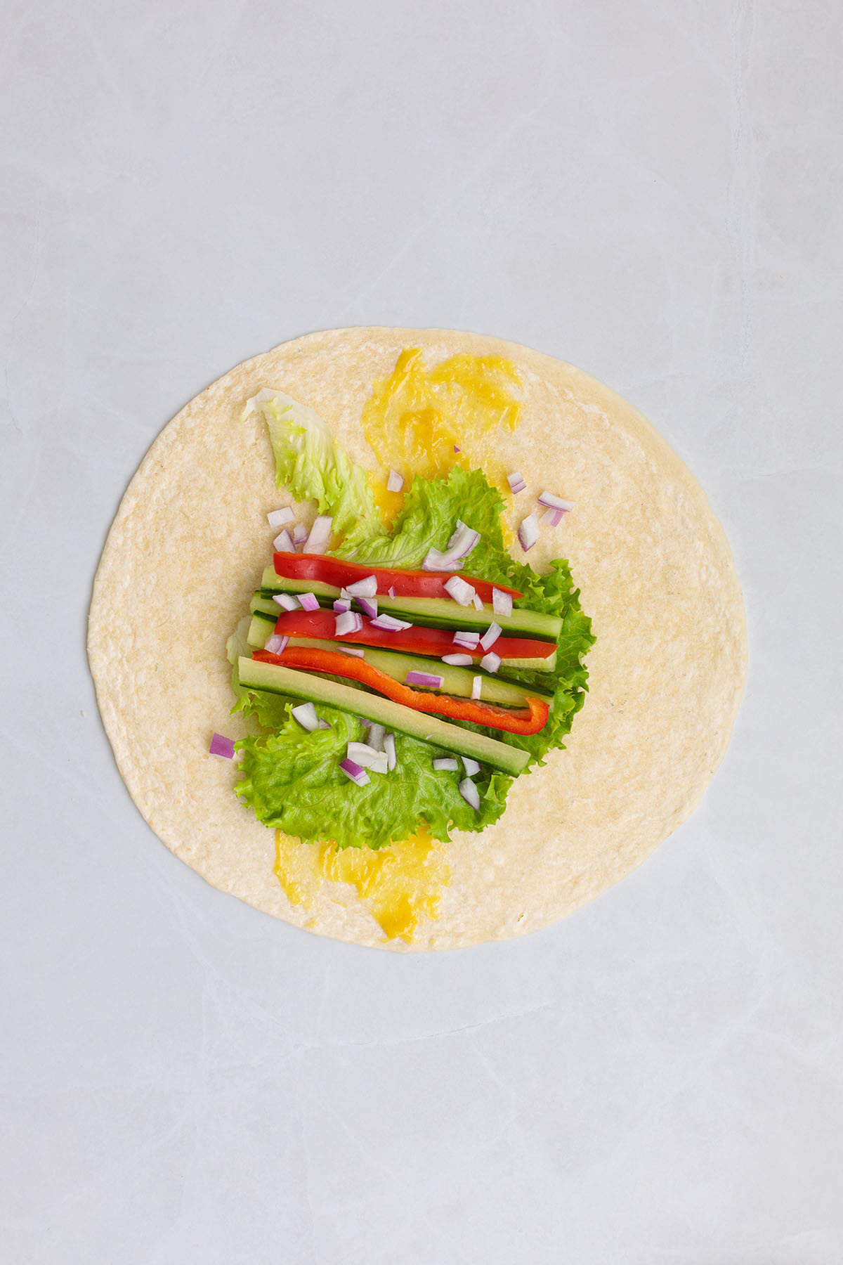 Flour tortilla with honey mustard sauce, lettuce, red peppers, cucumbers, and red onion.