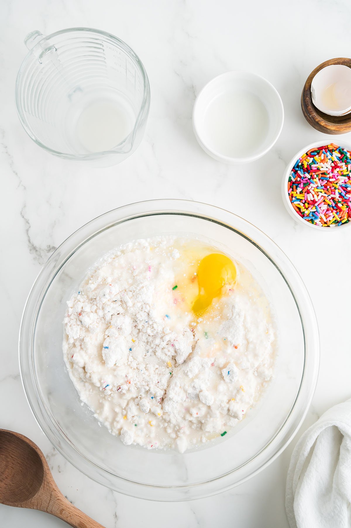 Funfetti cake mix, egg, milk, and vegetable oil in a glass mixing bowl.