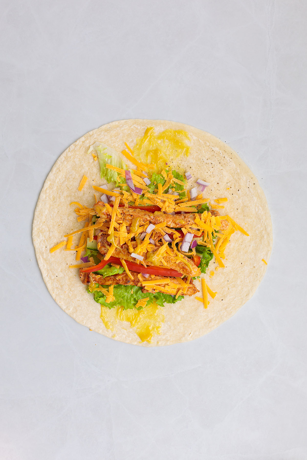 Honey mustard sauce, lettuce, red peppers, cucumbers, red onion, cheese, and chicken layered in a flour tortilla.