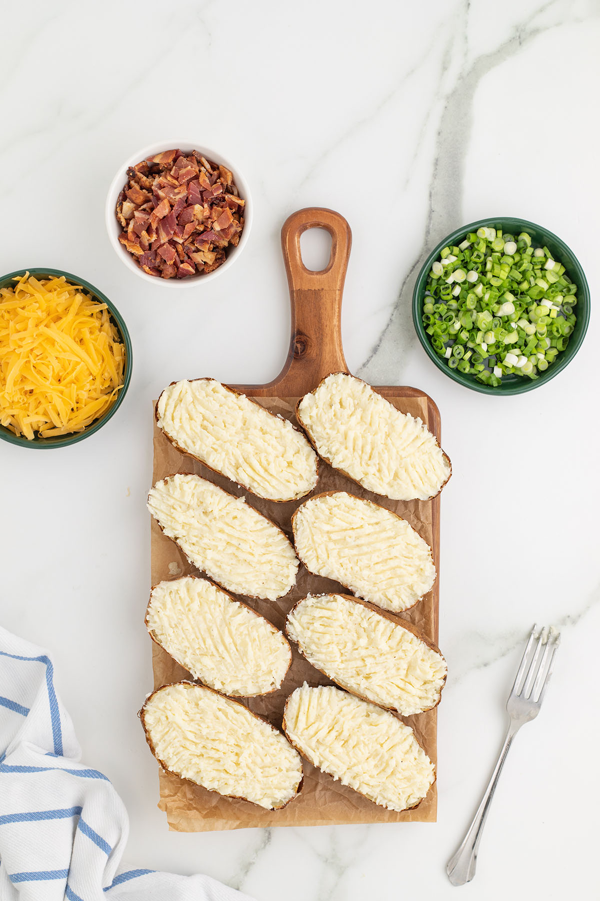 Mashed potato mixture spread into the potato skins on a wooden board.