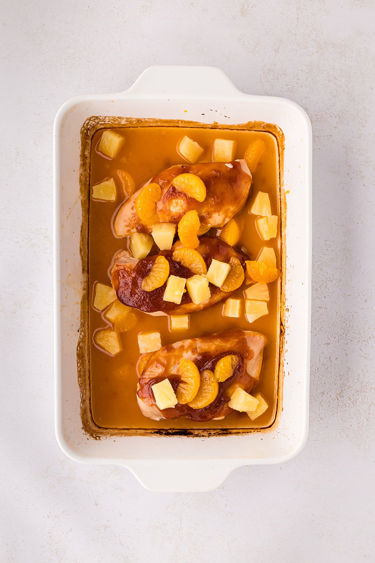 Pineapple chunks and mandarin orange slices are added to the chicken in the baking pan.