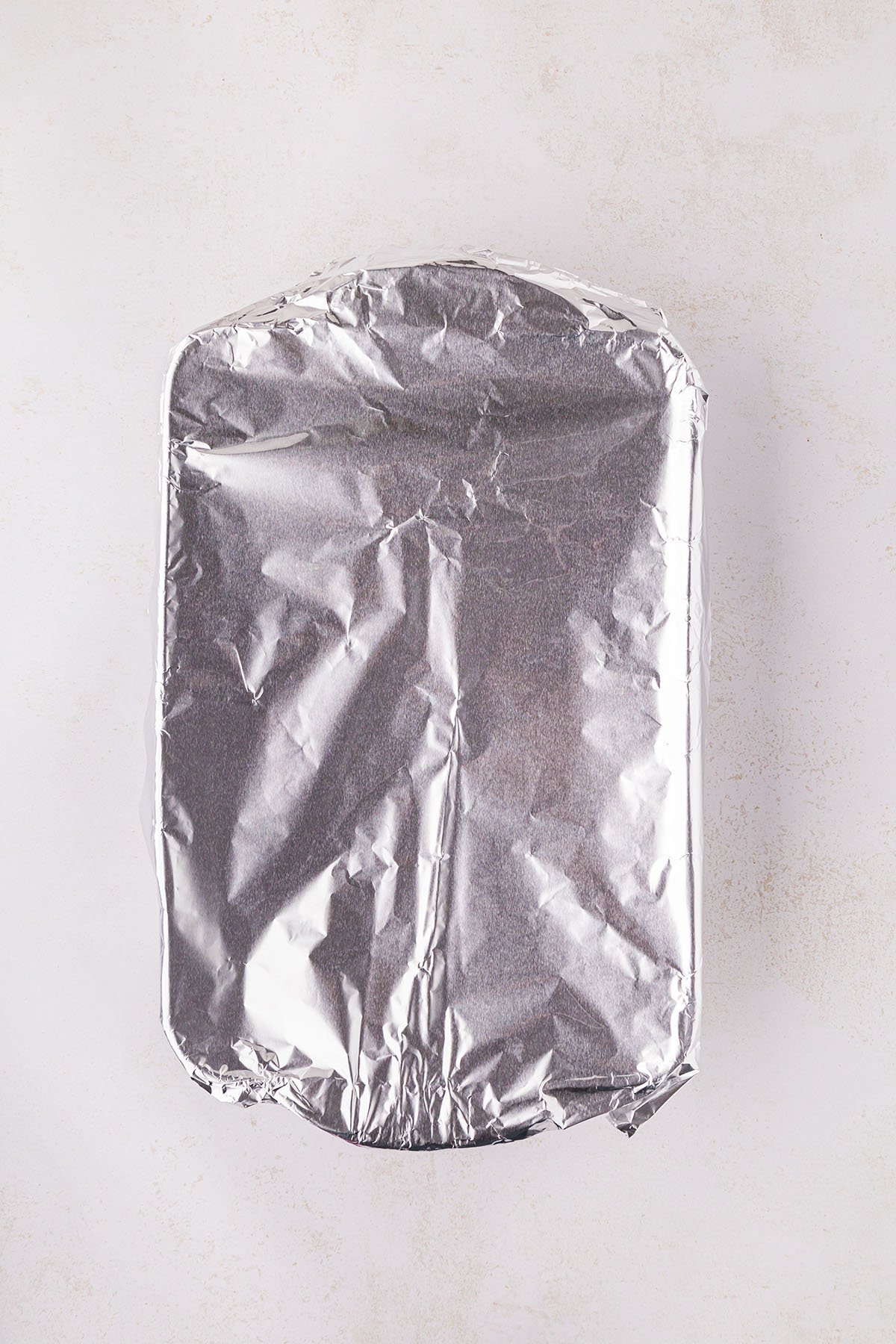 Raw chicken breasts in a baking pan, covered with pineapple juice, are wrapped in aluminum foil.