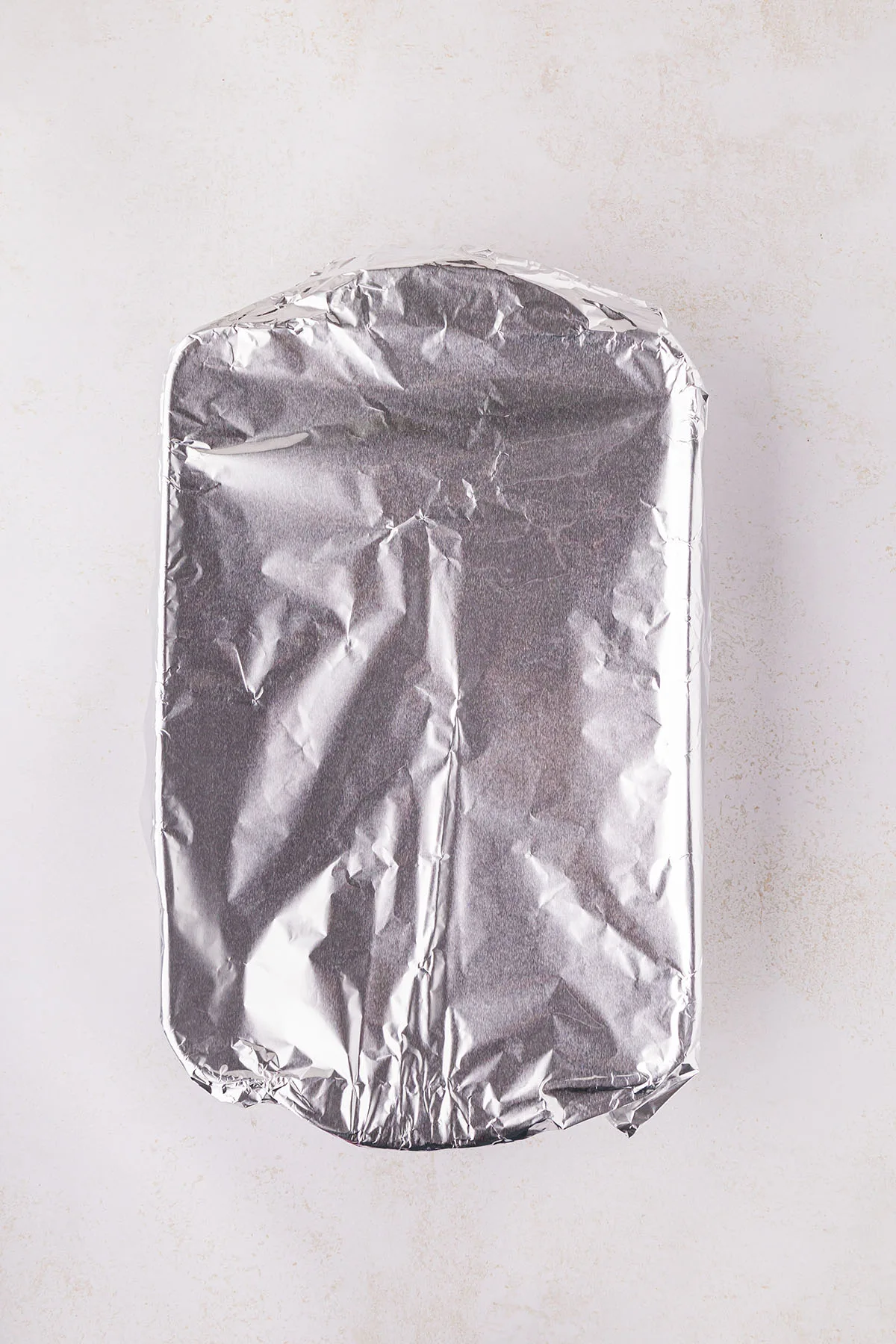 Raw chicken breasts in a baking pan, covered with pineapple juice, are wrapped in aluminum foil.