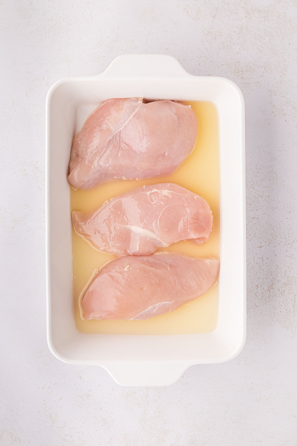 Raw chicken breasts in a baking pan with pineapple juice.
