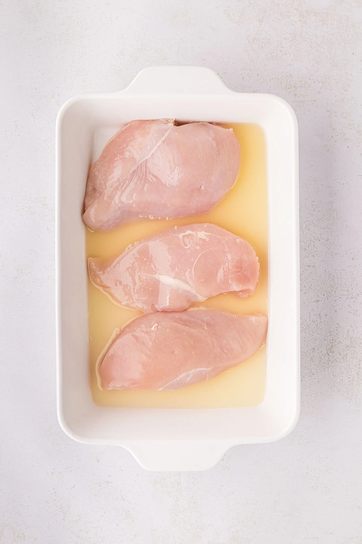 Raw chicken breasts in a baking pan with pineapple juice.
