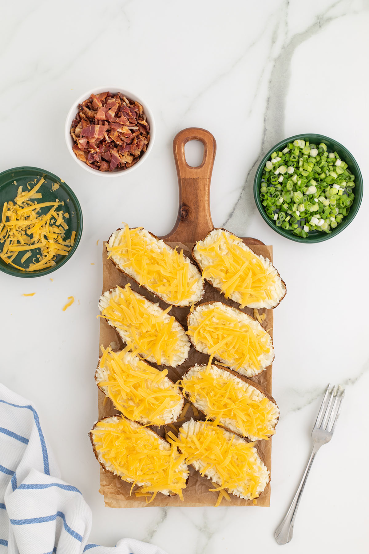 Shredded cheese spread over the mashed potato mixture in the potato skins on a wooden board.