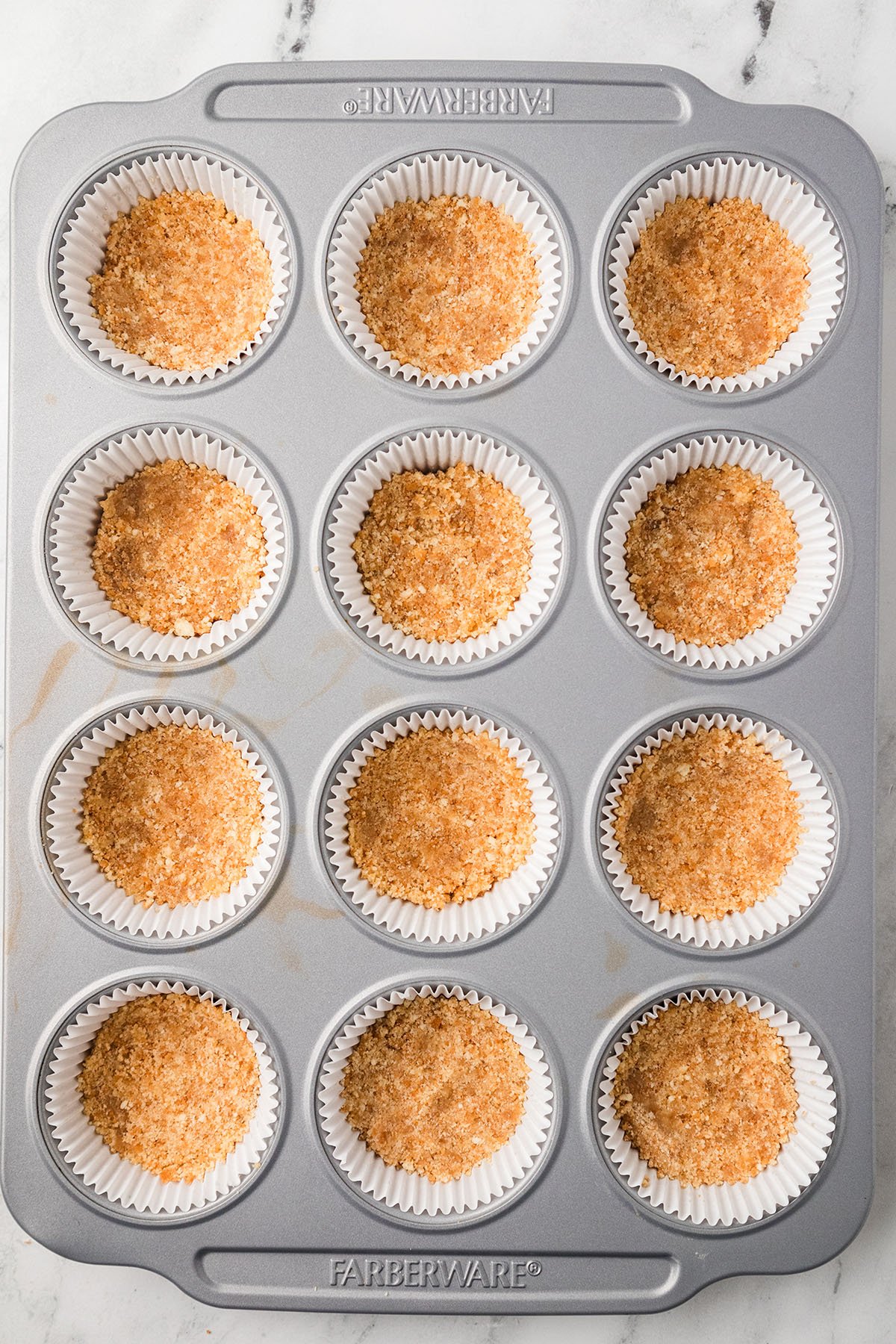 Vanilla wafer crust pressed into the bottom of a muffin pan lined with cupcake liners.