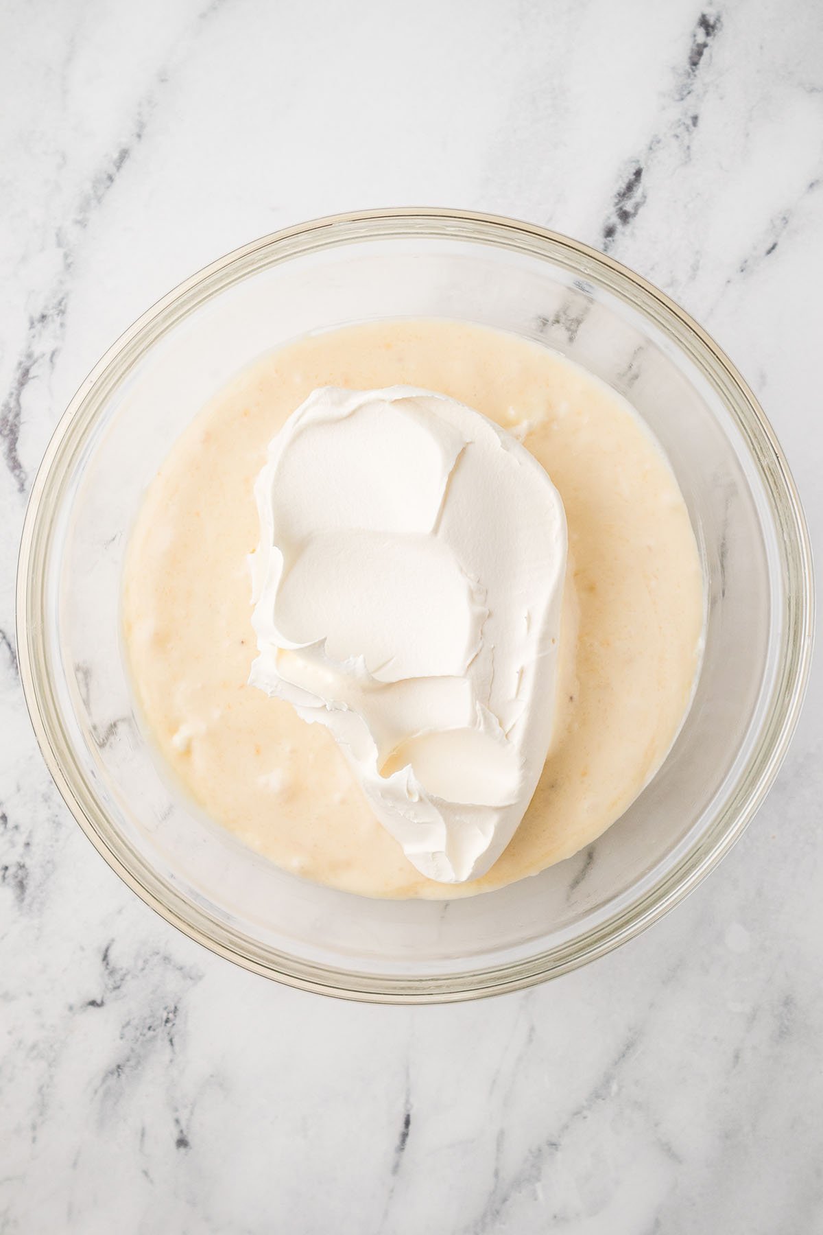 Whipped cream was added to the cream cheese mixture in the glass mixing bowl.