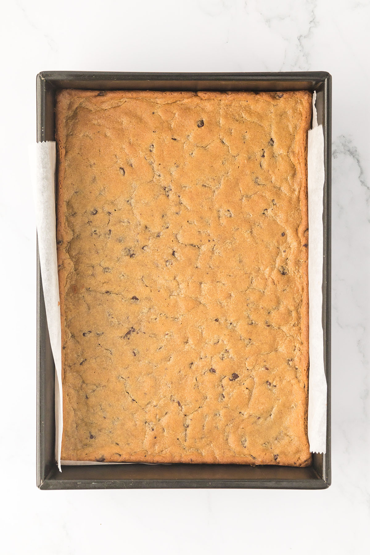 Baked chocolate chip cookie dough layer in the baking pan.