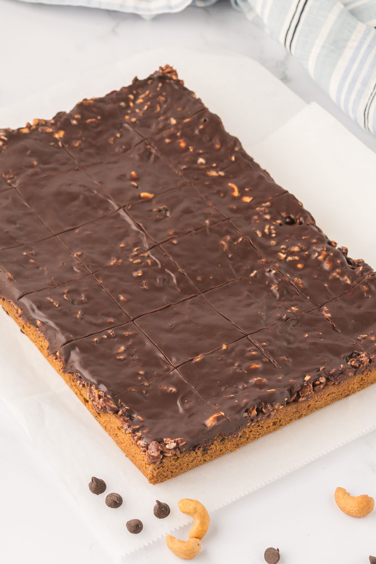 Caramel Cashew Bars with chocolate caramel topping on parchment paper cooling.