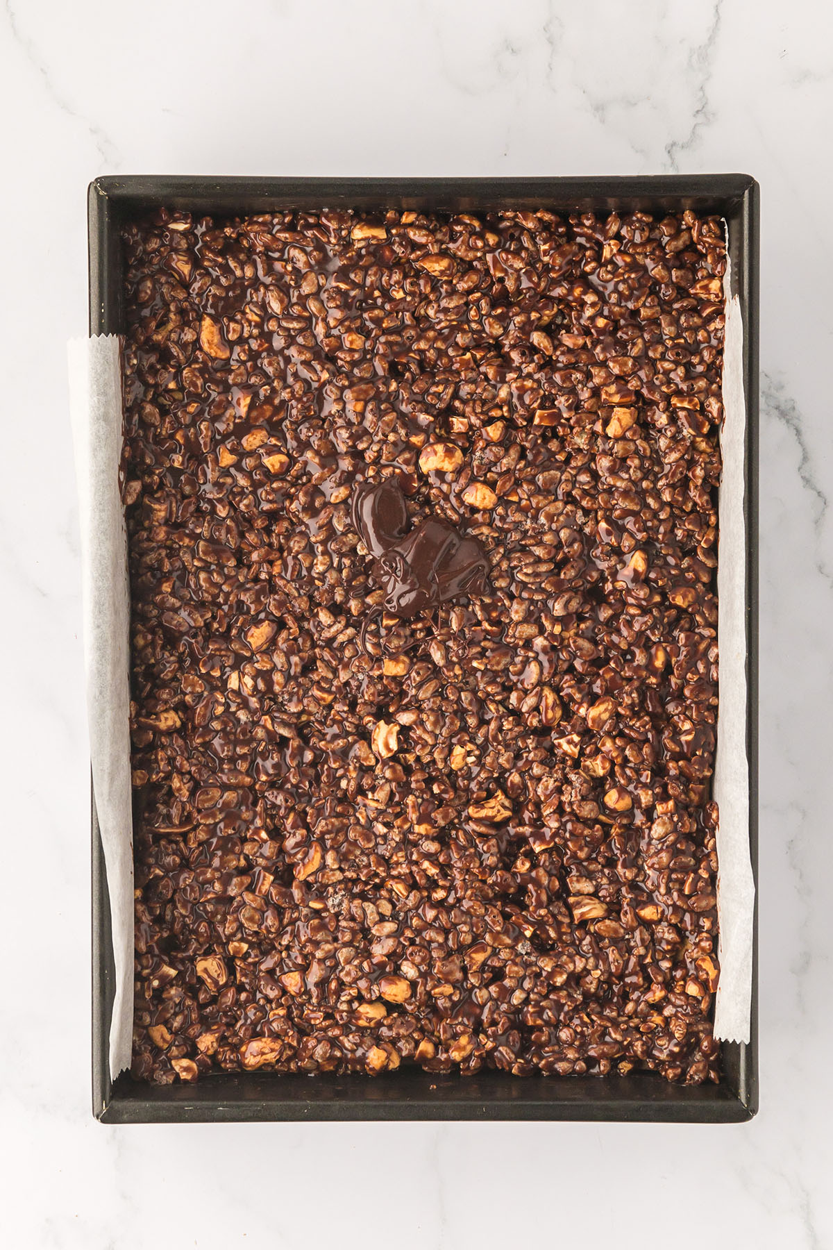 Caramel Cashew cereal pressed over the chocolate chip cookie layer in the baking pan.