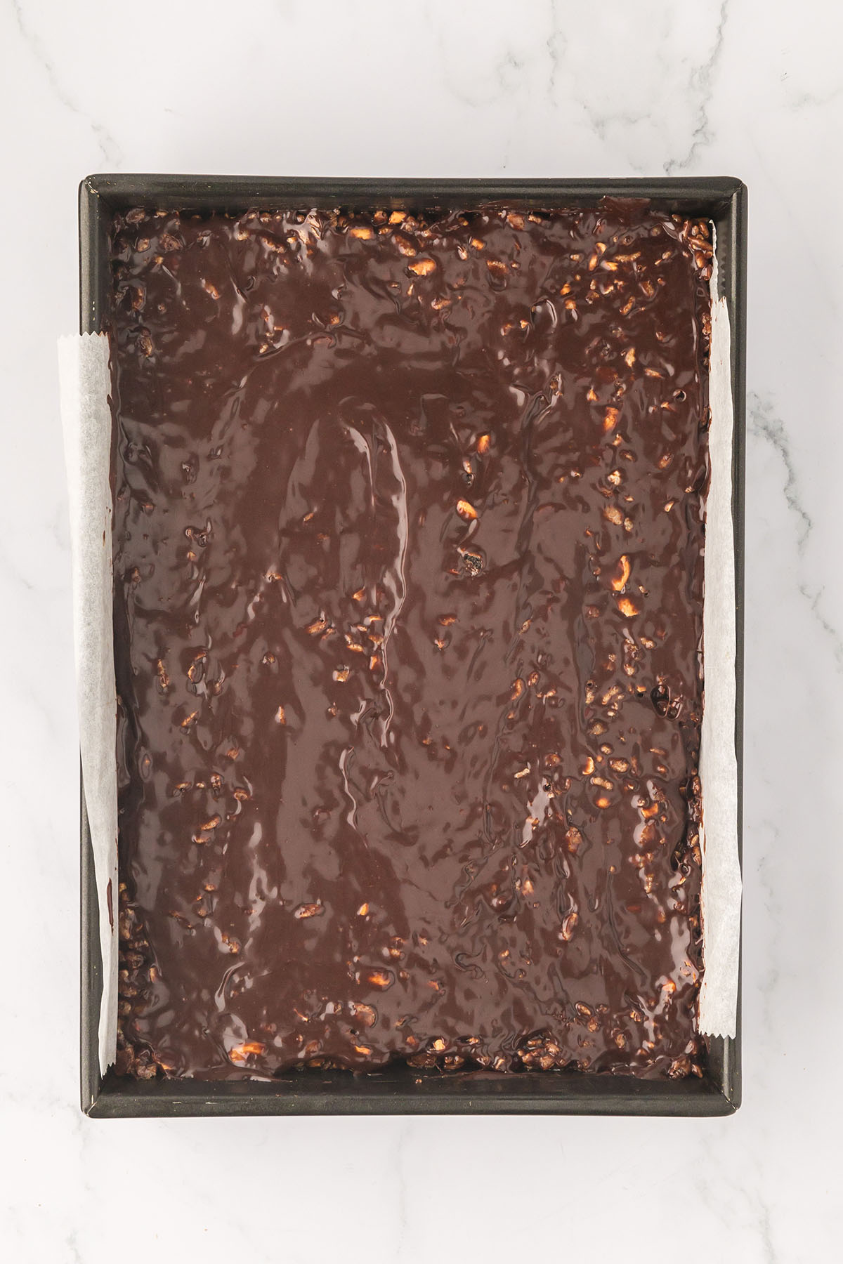 Chocolate caramel topping spread over the caramel cashew bars in the baking pan.