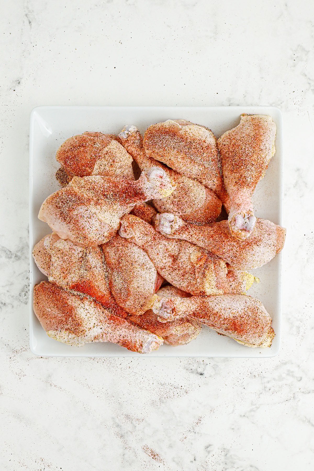 Drumsticks seasoned with garlic powder, onion powder, smoked paprika, chili powder, salt, and pepper on a square plate.
