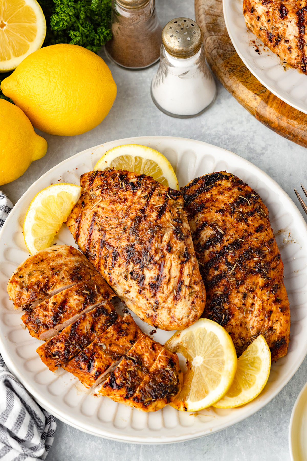 Three Lemon Herb Chicken breasts on a plate, with one sliced.