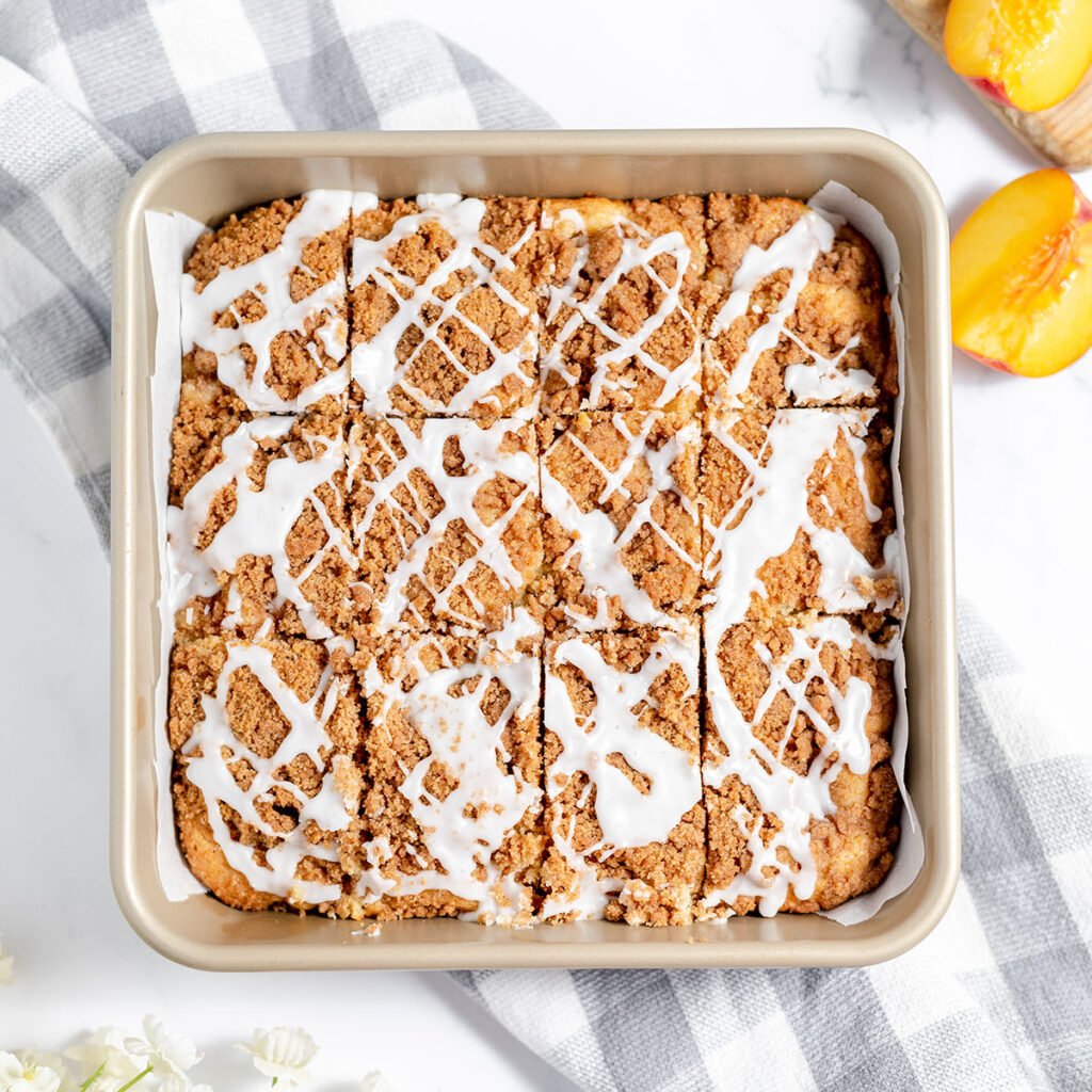 Peach coffee cake drizzled with icing in a square baking pa.