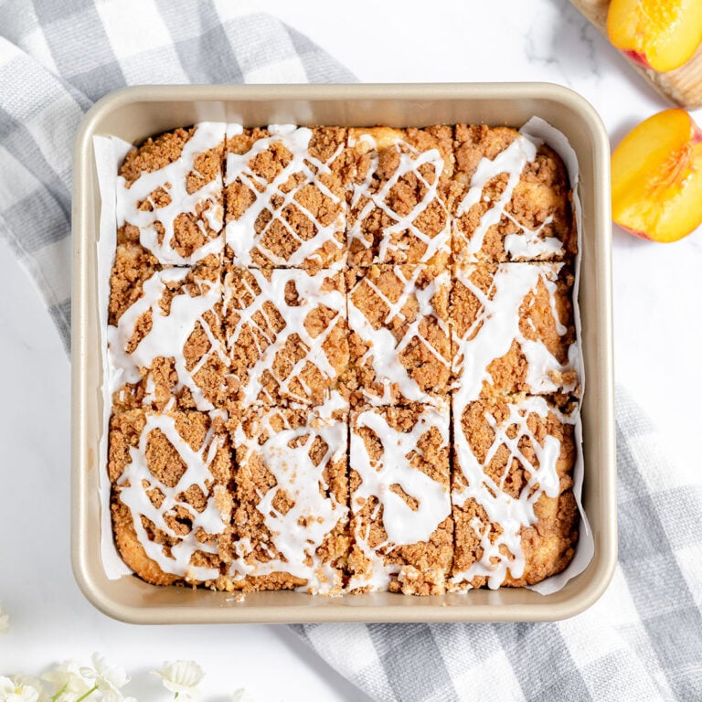 Peach coffee cake drizzled with icing in a square baking pa.