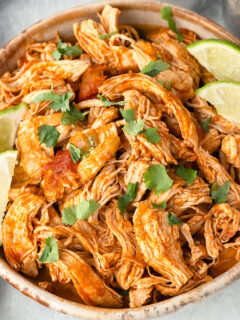 Shredded Mexican Chicken in a bowl with lime slices.