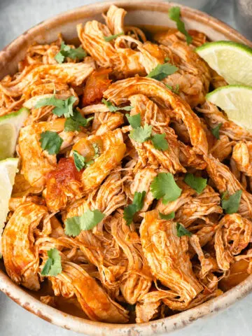 Shredded Mexican Chicken in a bowl with lime slices.