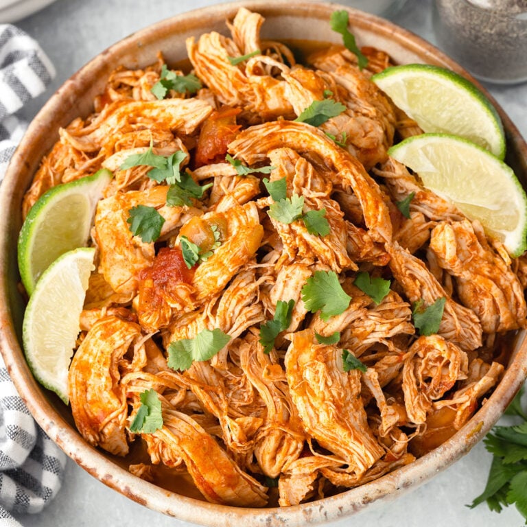 Shredded Mexican Chicken in a bowl with lime slices.