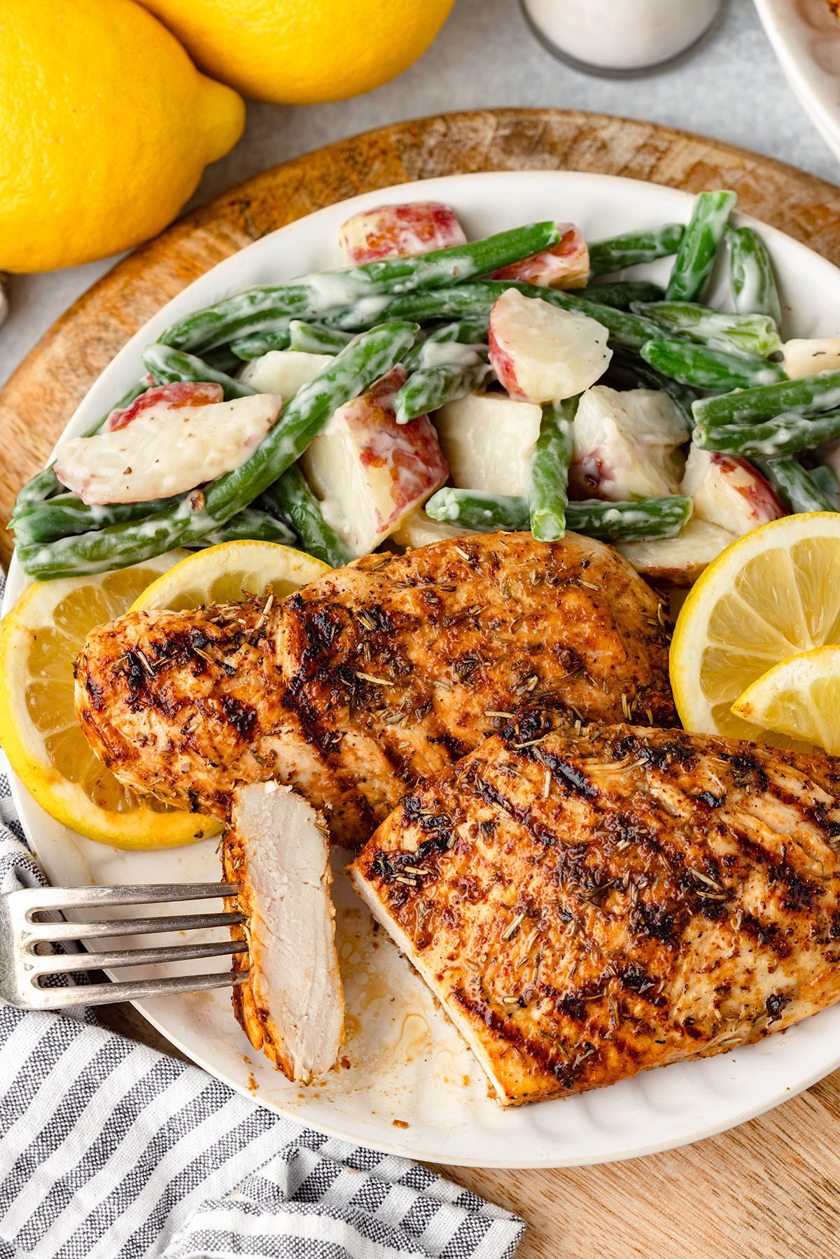 Lemon Herb Chicken served on a white plate with lemon slices, potatoes, and asparagus. 