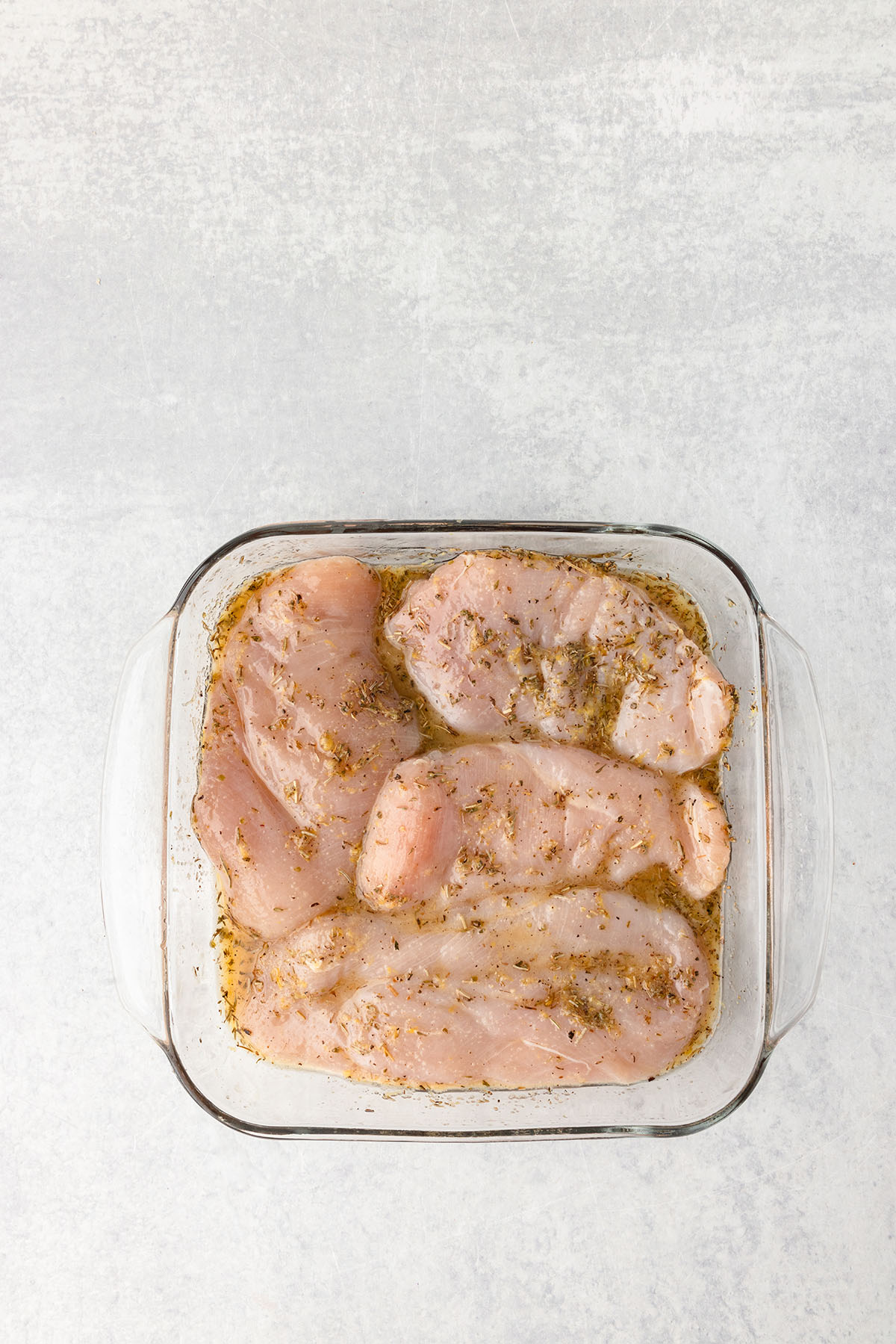 The lemon herb marinade is poured over the chicken breast in a glass dish.
