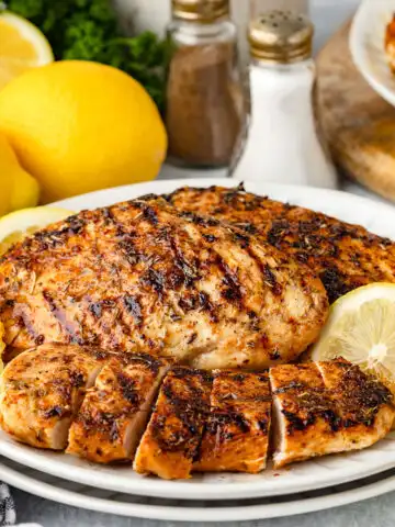 Lemon herb chicken served on a white plate with lemon slices.
