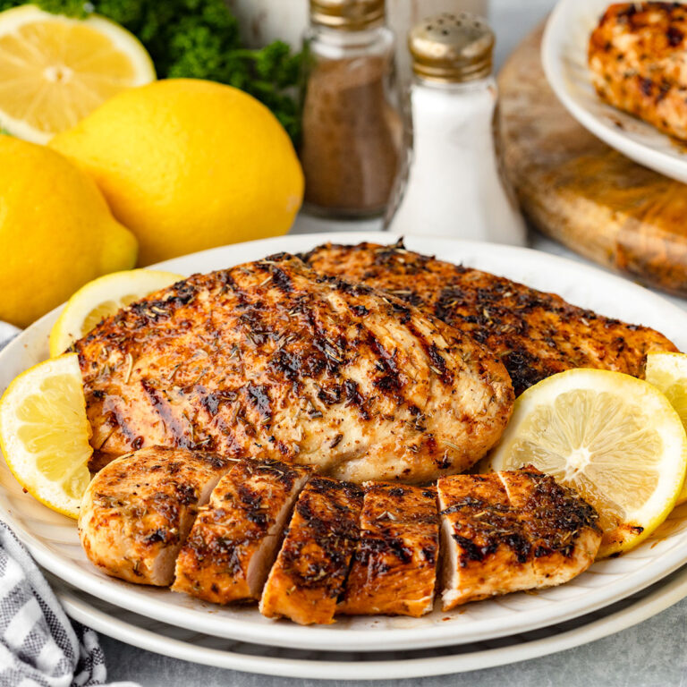 Lemon herb chicken served on a white plate with lemon slices.