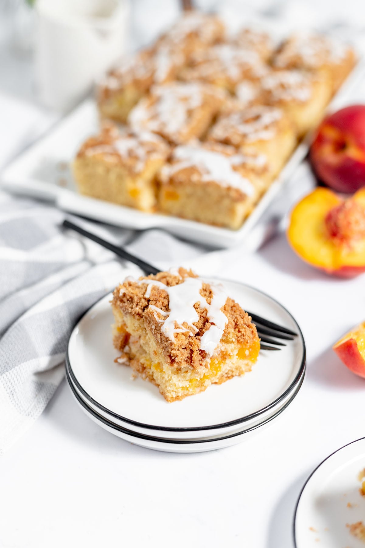 A slice of peach coffee cake drizzled with icing on a white plate with a fork.
