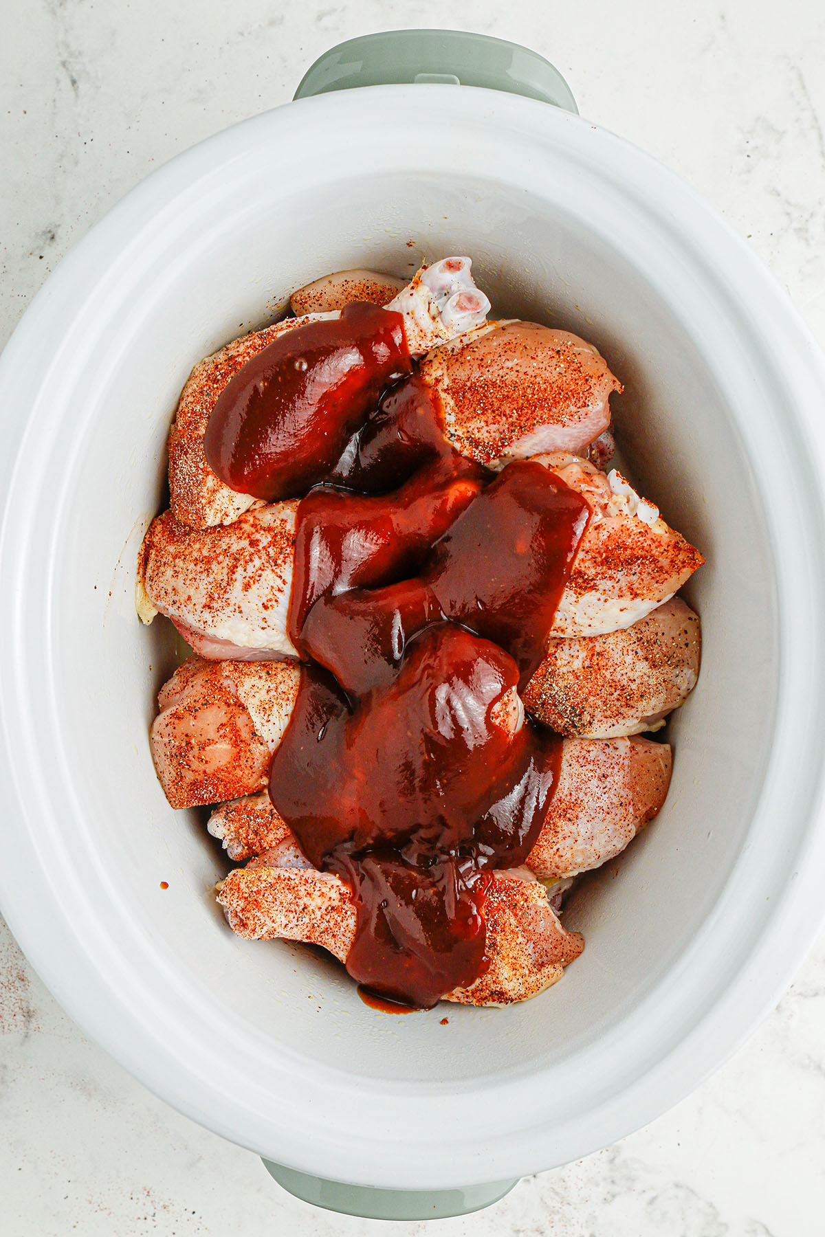 Seasoned drumsticks topped with BBQ sauce in the slow cooker.