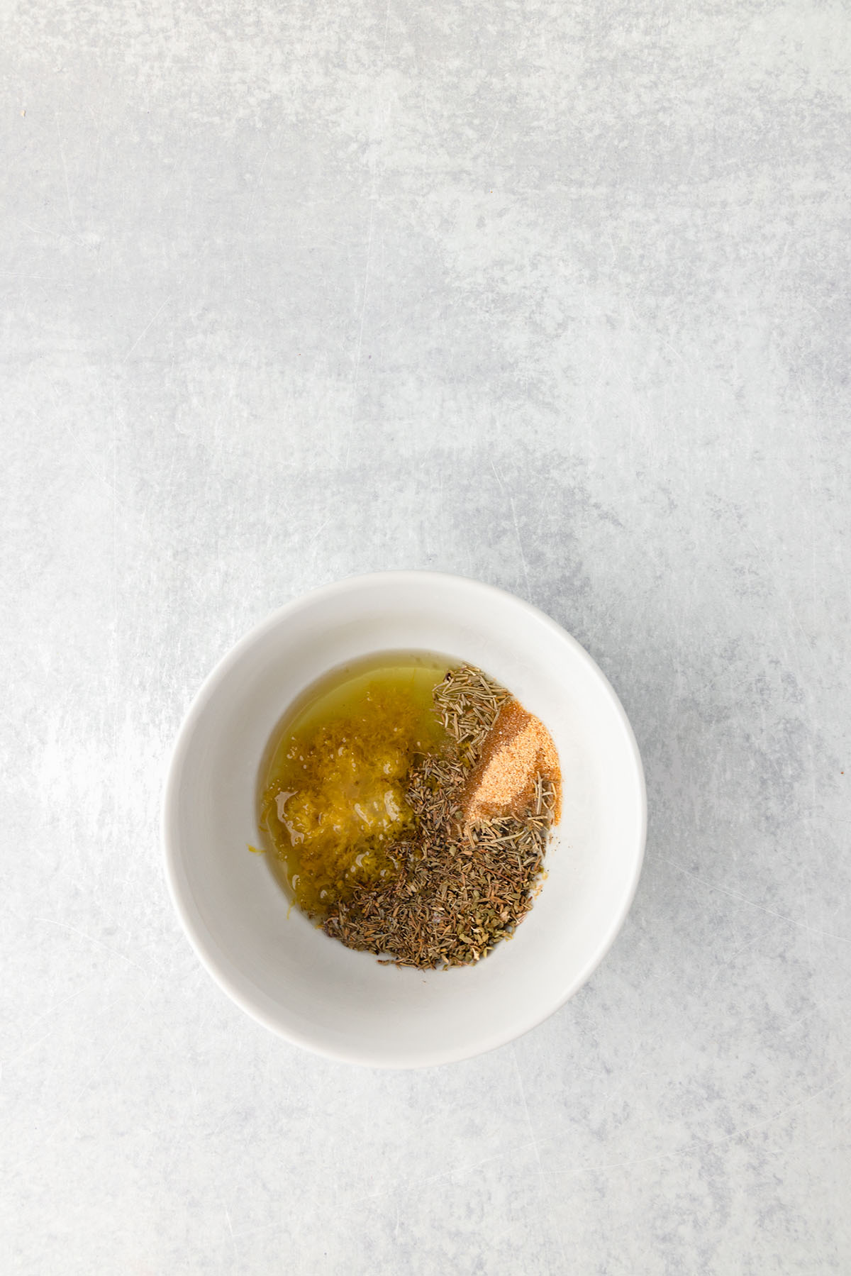 Avocado oil, lemon juice, lemon zest, garlic powder, dried herbs, salt, and pepper in a small glass bowl.